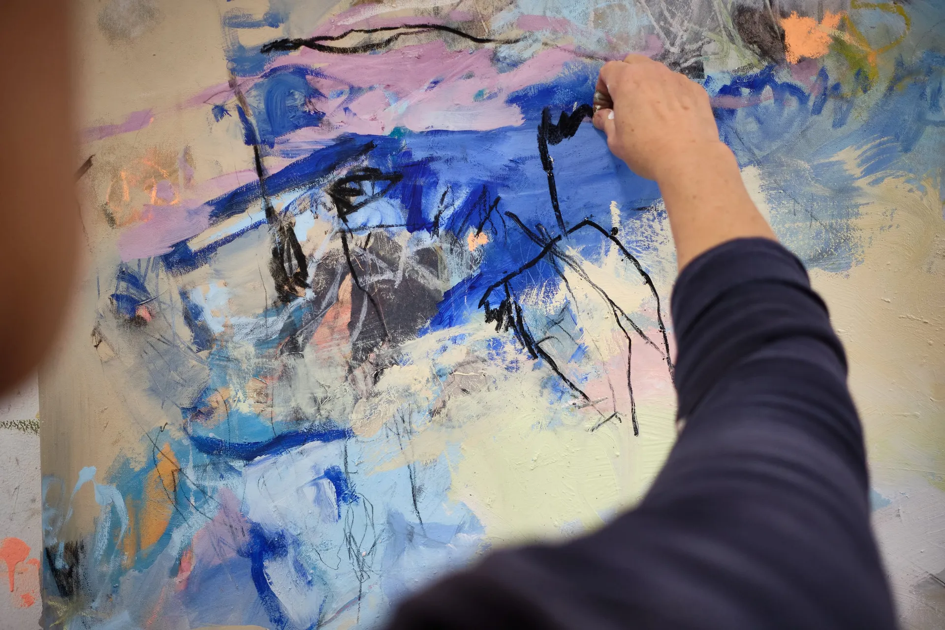 Eine Hand malt mit schwarzem Strich auf eine große Leinwand in Blau und Rosa.