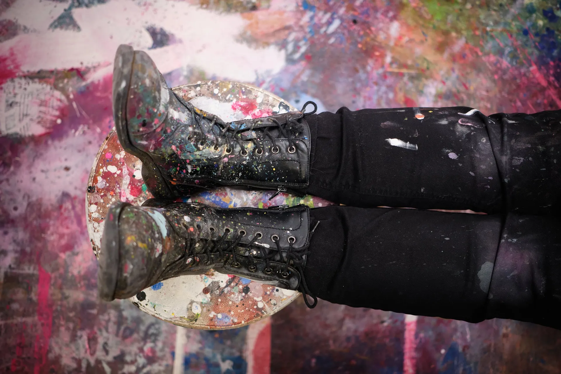 Zwei farbbekleckerte Stiefel stehen auf einer Palette voller Farbreste.