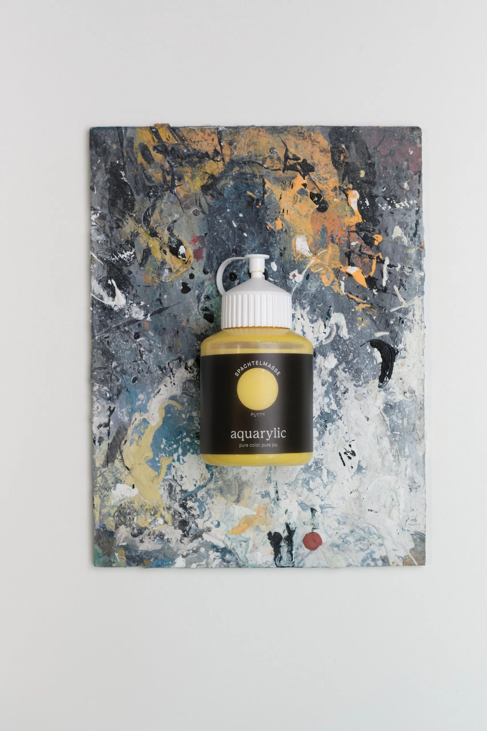 Eine Flasche goldene Farbe liegt auf einer bemalten Platte vor weißem Hintergrund.