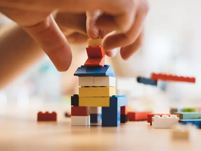 Hände setzen eine Figur auf einen Turm aus bunten Lego-Steinen.