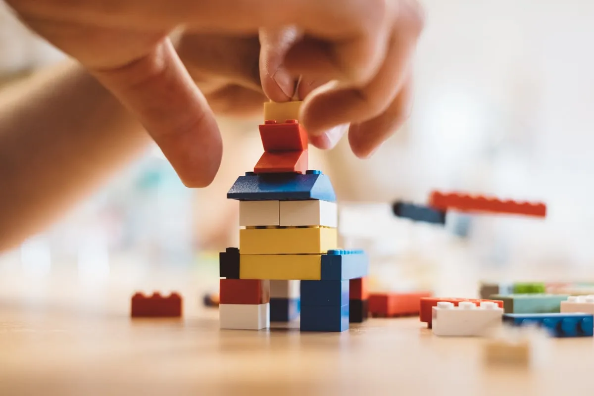 Hände setzen eine Figur auf einen Turm aus bunten Lego-Steinen.
