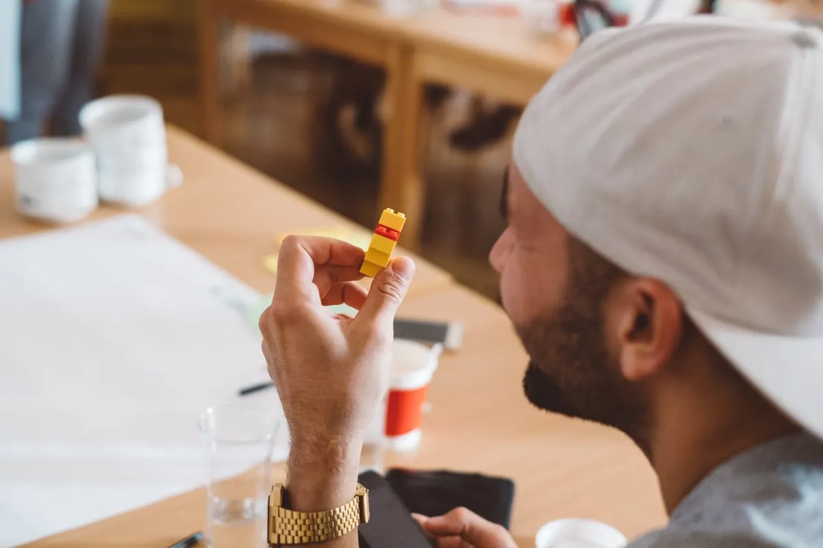 Ein Teilnehmer mit Kappe hält eine kleine Lego-Figur in der Hand, vor ihm liegt ein Blatt Papier.