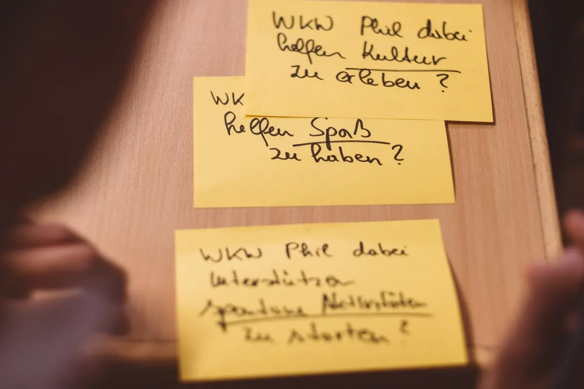Gelbe Haftnotizen mit handschriftlichen Fragen kleben an einer Holzwand.