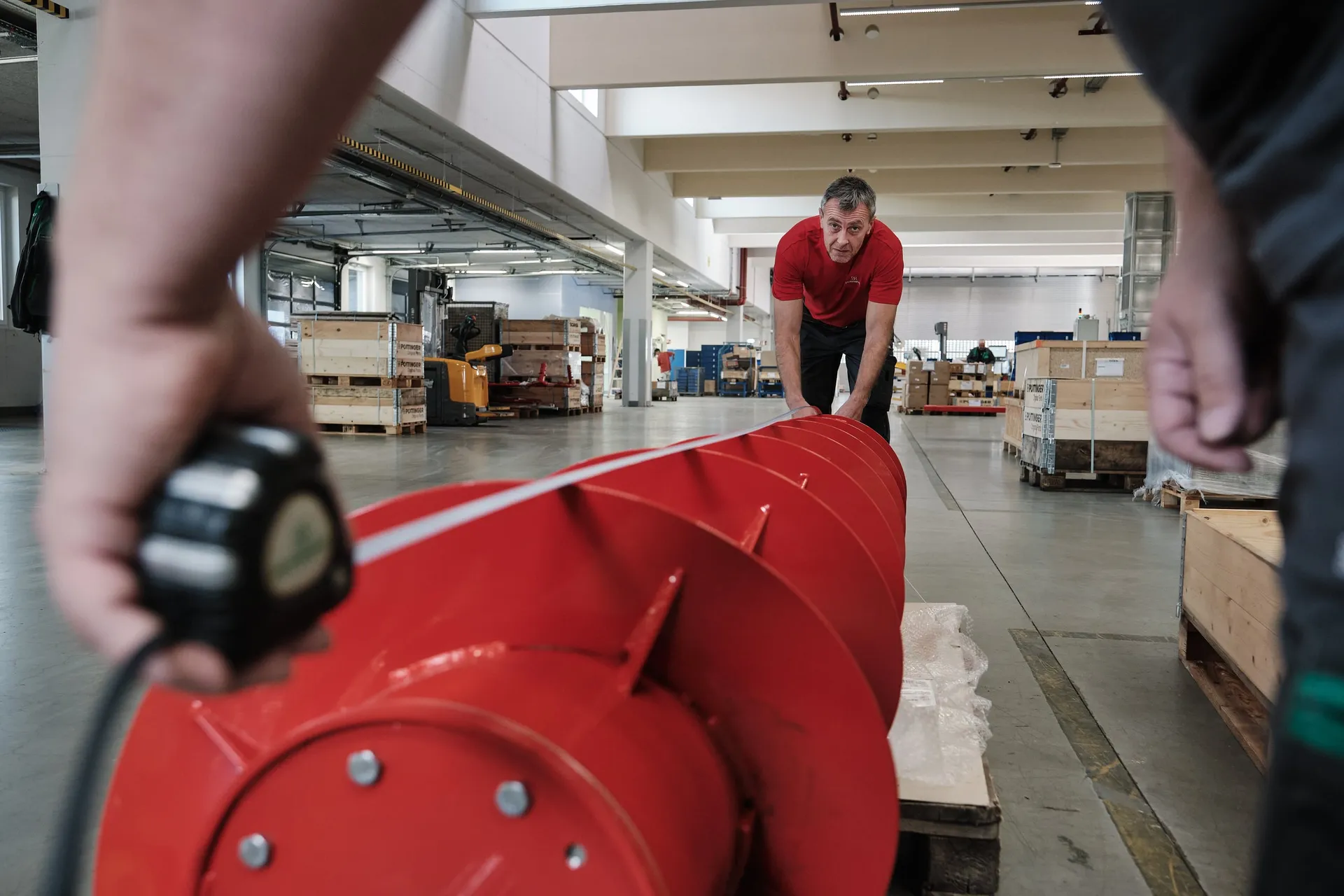 Ein Mitarbeiter schiebt in der Halle ein großes rotes Schneckenteil, im Vordergrund hält eine Hand ein Messgerät.