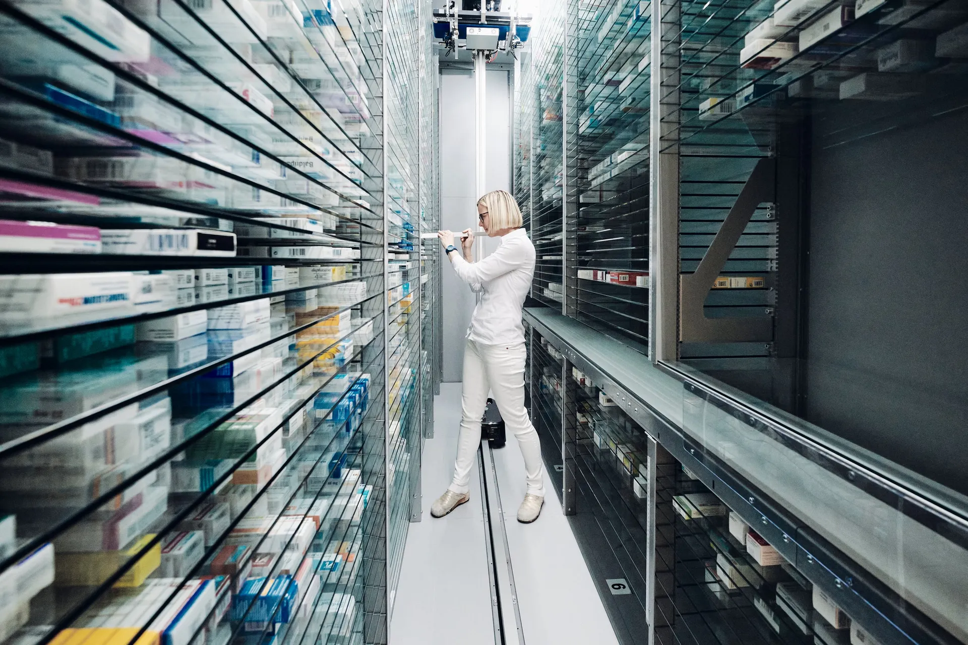 Eine Mitarbeiterin steht im Kommissionierautomaten zwischen dicht gefüllten Medikamentenregalen.