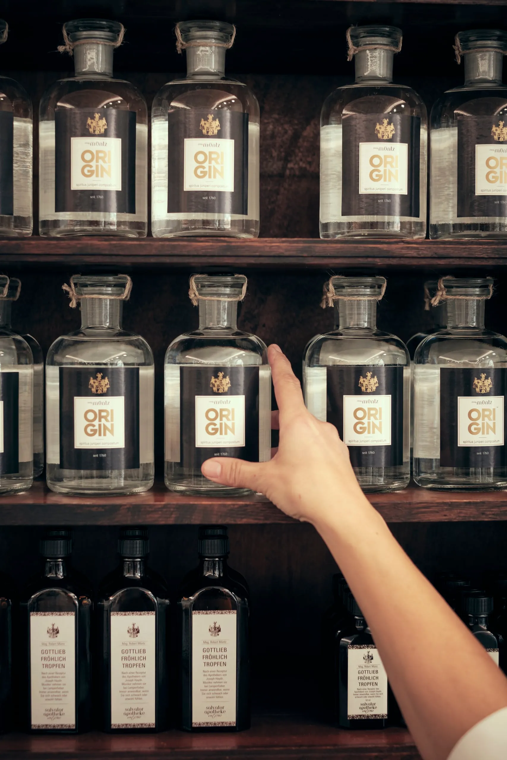 Eine Hand zeigt auf eine von mehreren Apothekerflaschen im Regal.